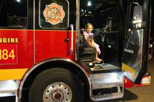 Girl sits in fire truck.